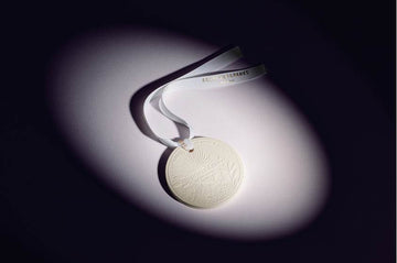 Mystic Bliss scented round ceramic ornament with white ribbon on dark background